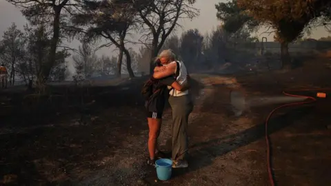 Reuters Marina Kalogerakou, 24, hugs her aunt Eleonora Zoakou, 48, as a wildfire rages in Penteli, Greece, August 12, 2024