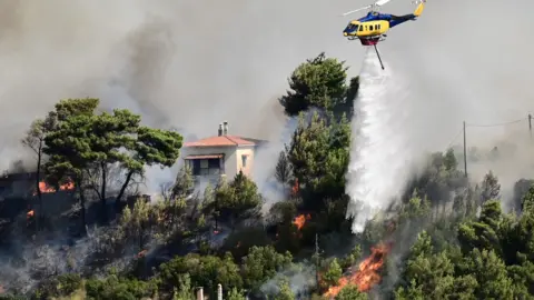 Reuters A helicopter flies, dropping water on a fire burning near a house