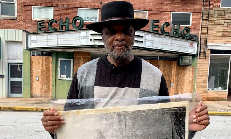The Rev. David Kennedy stands outside the former Echo Theater, holding a photo of his great-great-uncle's lynching.