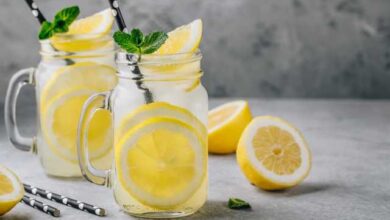 Two jars of water with lemon slices and straws against a gray background