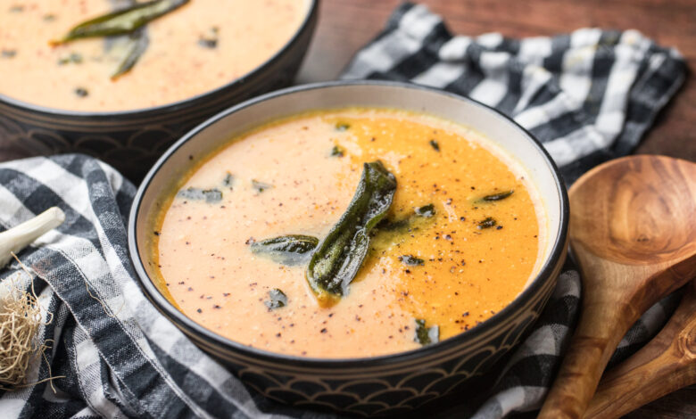 Bowls of butternut squash soup with fried sage, wooden spoons