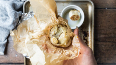 Hand holding a roasted head of garlic wrapped in parchment paper