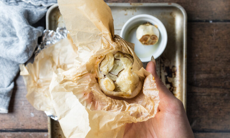Hand holding a roasted head of garlic wrapped in parchment paper