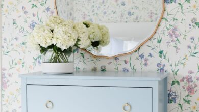 A bedroom with floral wallpaper and a dresser painted in a slate Blue color