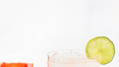 A paloma cocktail with a lime garnish and a slice off grapefruit in the background