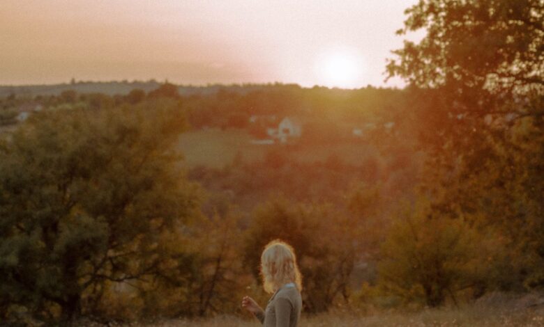 Mental health. Woman standing in an open field looking over a hillside at sunset.