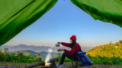 View from inside green tent of woman enjoying hot drink in front of campfire