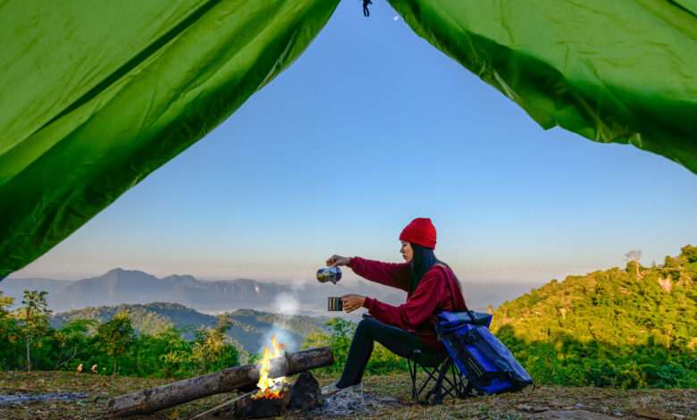 View from inside green tent of woman enjoying hot drink in front of campfire