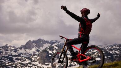 Male mountain biker stands with arms outstretched on mountaintop astride red bike