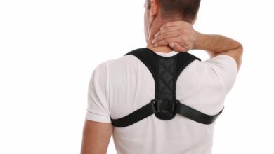 Man in white tee shirt wearing posture corrector harness and holding back of neck.