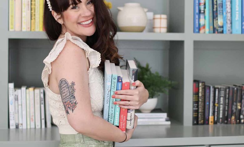 Woman holding a stack of books in front of bookshelf
