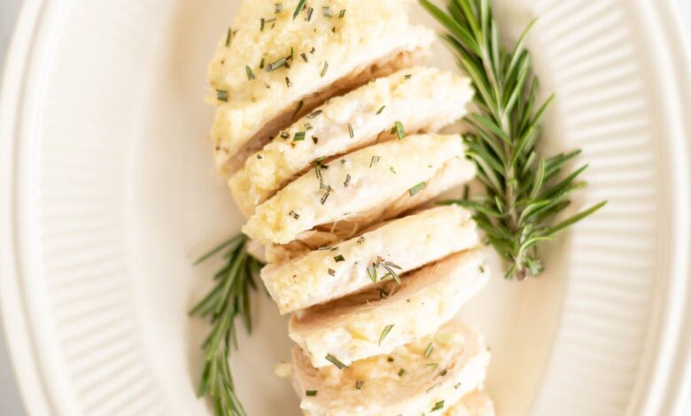 Sliced mayo chicken, garnished with fresh rosemary on an oval platter.