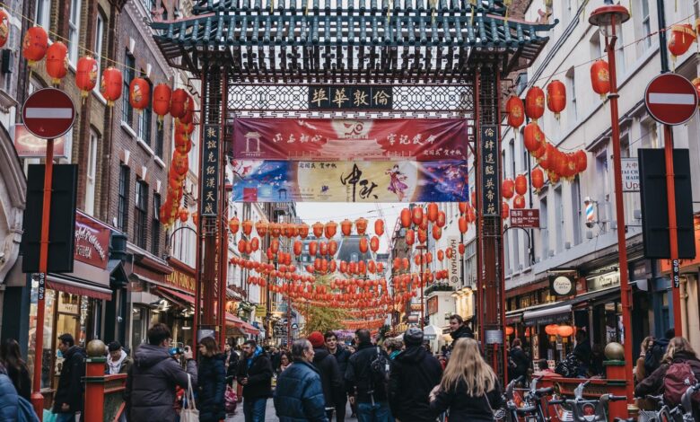 London, UK - November 24, 2019: People walking by Chinatown Gate in Chinatown, London. Chinatown is home to a large East Asian community and is famous for its eateries and events. Selective focus.