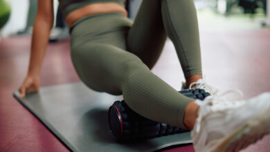 Woman uses foam roller on leg while exercising in a gym.