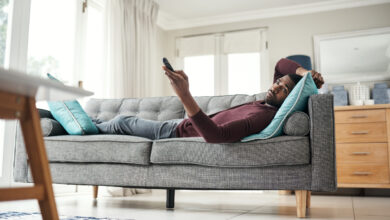 Shot of a man using a remote control while lying on the couch at home.