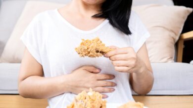 Woman eating fried chicken holding stomach as if in pain.