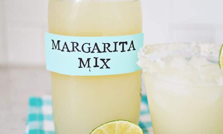 Margarita mix in a jar with a glass of margarita and a lime next to it