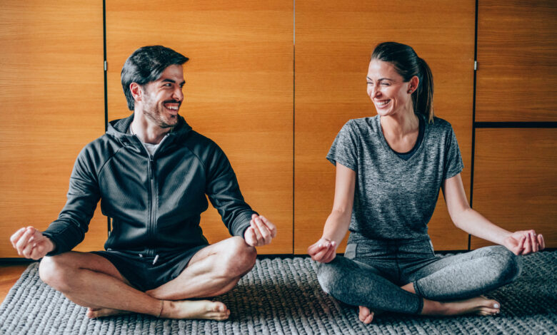 Couple sitting in lotus position, looking at each other and laughing.
