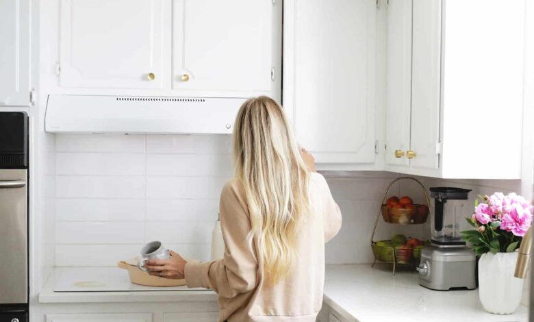 a blonde woman standing in a white kitchen holding a coffee mug