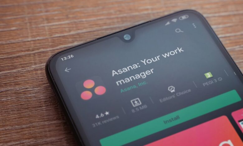 Asana app play store page on the display of a black mobile smartphone on wooden background