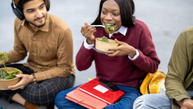 College students eating salad sitting on the ground and smiling.