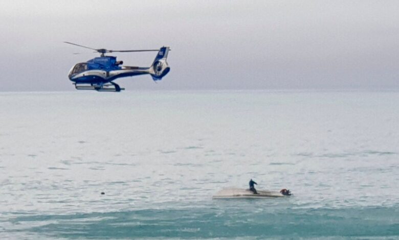 Helicopter flies above an upturned boat with a survivor on board