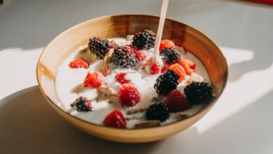 Dairy free milk pouring into a bowl of whole grain cereal, raspberries and blackberries.