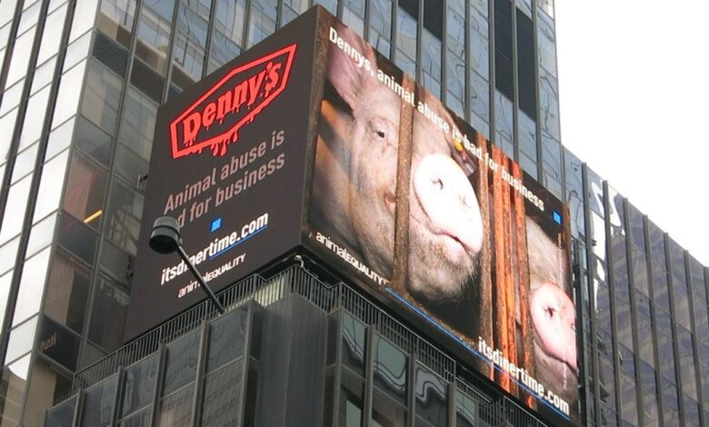A digital billboard featuring a pig peering through the bars of a crate. The text reads, "Denny