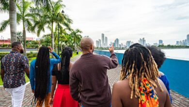 Local Tour Guide Walking and Pointing Toward the Skyline with a Group of Cheerful, Fashionable Afro-Descendant Tourists Together with a View of Panama City