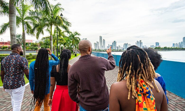 Local Tour Guide Walking and Pointing Toward the Skyline with a Group of Cheerful, Fashionable Afro-Descendant Tourists Together with a View of Panama City